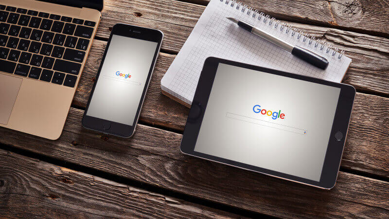 iphone and ipad on a wooden desk with Google search on the screens