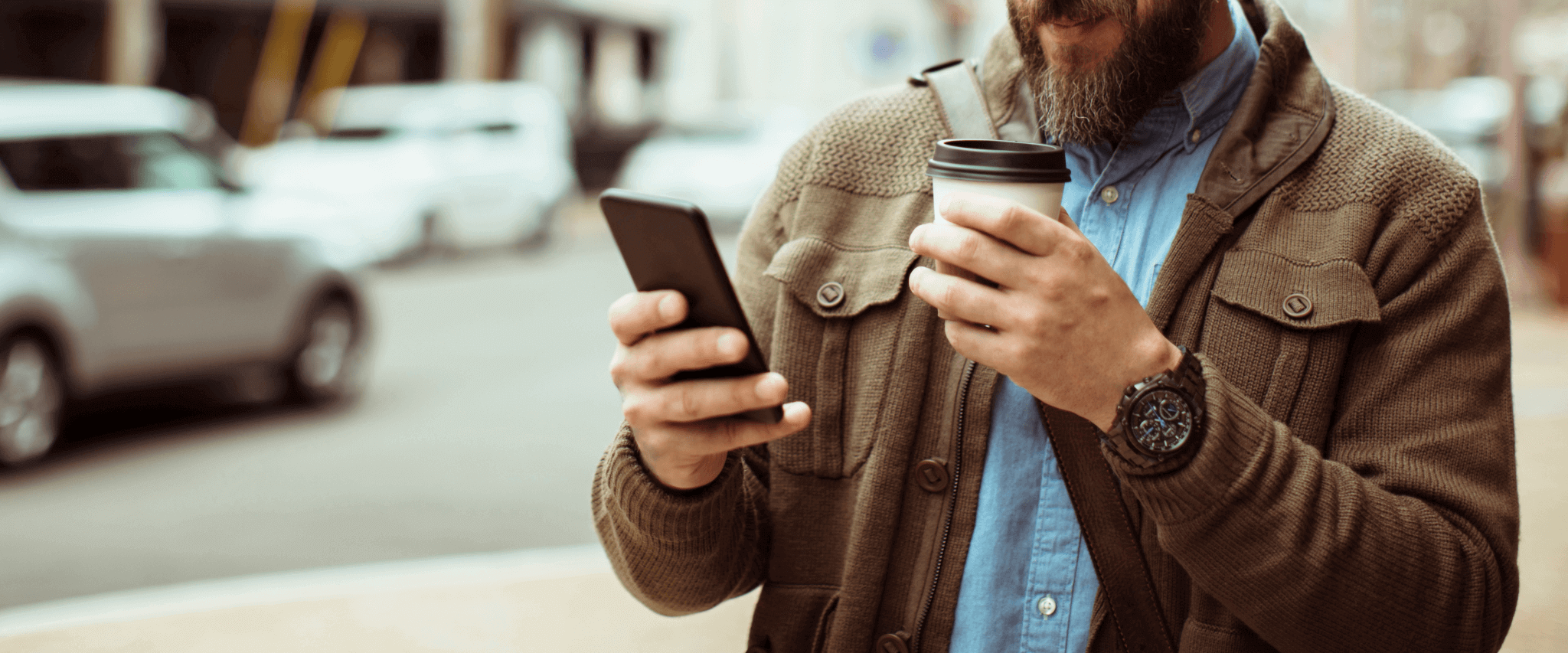 man using iphone with coffee in hand